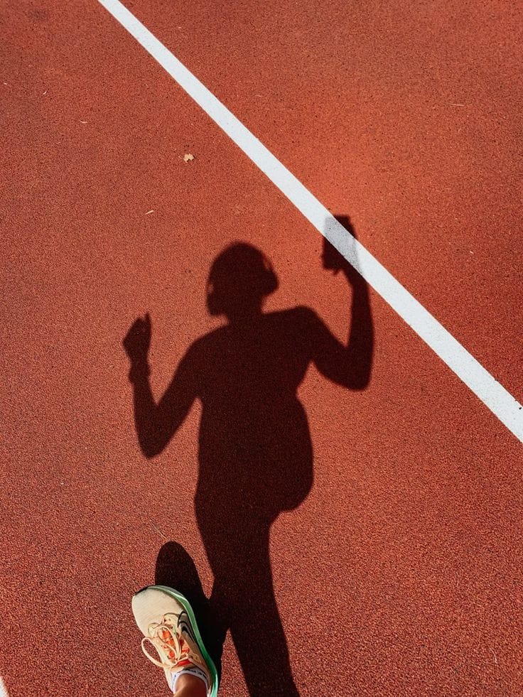 Dynamic shadow of a runner celebrating on a red track, embodying the high-energy active lifestyle promoted by Healing Factor.